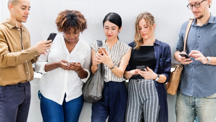 Five people standing in a row looking at their mobile phones