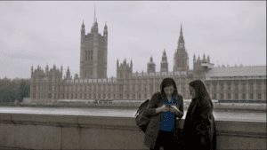 Two women stand infant of the house of parliament looking at a phone