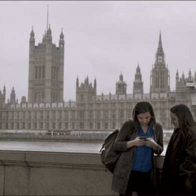 Two women stand infant of the house of parliament looking at a phone