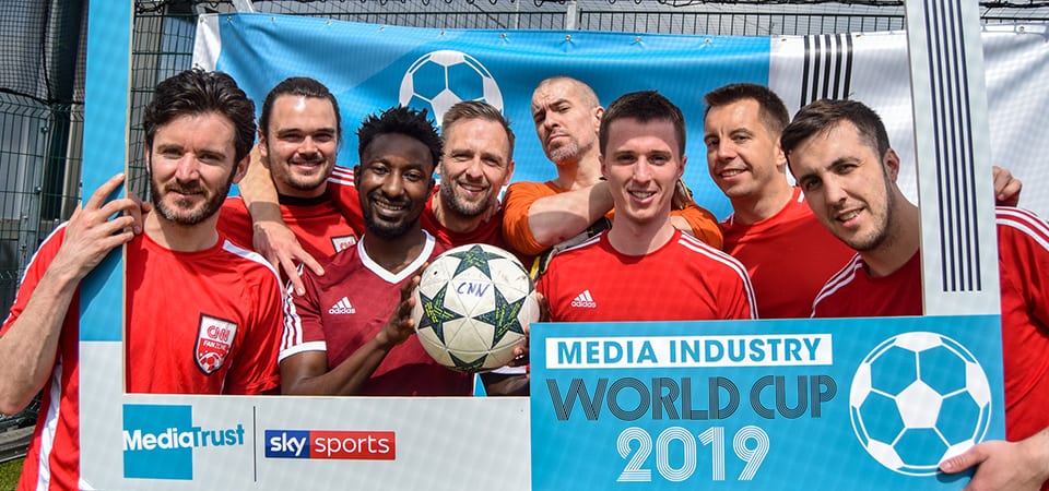 Group of men in football shirts hold a World Cup 2019 cut out frame and a football