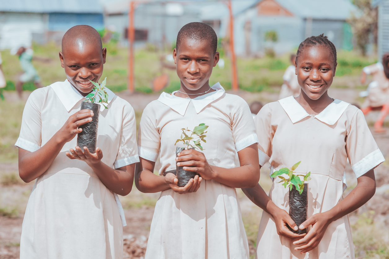 Three young people holding plants and smiling.