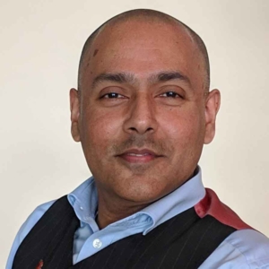 A picture of Kamran Mallick, CEO at Disability Rights UK, wearing a blue shirt and navy pinstriped waistcoat, smiling slightly into the camera.