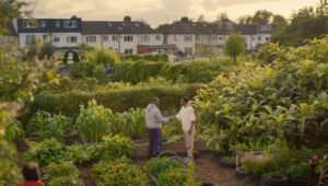 A young person shaking another person's hand in a large garden. There are houses in the back.
