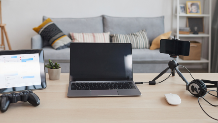 A streaming set up, showing a tablet, a joypad, a laptop, a camera on a tripod, a mouse and headphones.