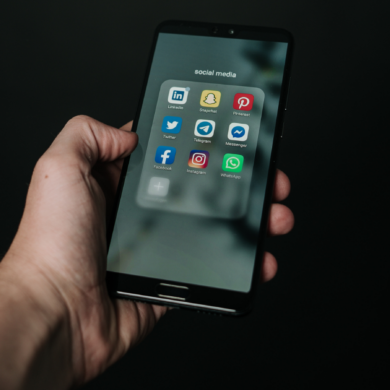 A person holding a mobile phone, showing a 'Social media' folder with the apps for LinkedIn, Snapchat, Pinterest, Twitter, Telegram, Messenger, Facebook, Instagram and WhatsApp.