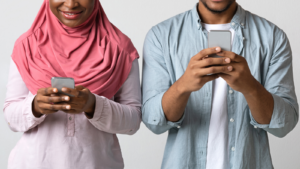 Two people stood next to each other, looking at mobile phones in their hands.