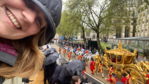 Hebe smiling for a photo in the rain as the Gold State Coach, with guards, drives through the crowds.
