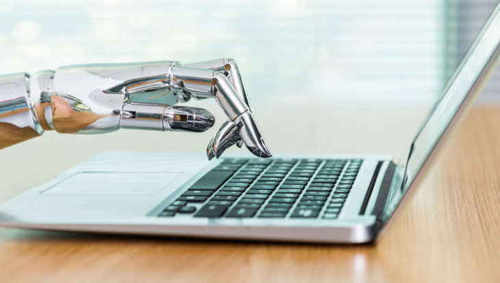 A silver, robotic hand typing on a laptop.