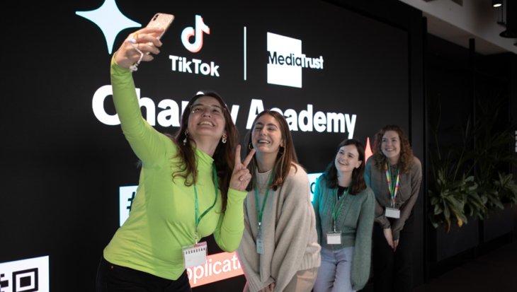 People posing for a selfie in front of the TikTok Charity Academy logo.
