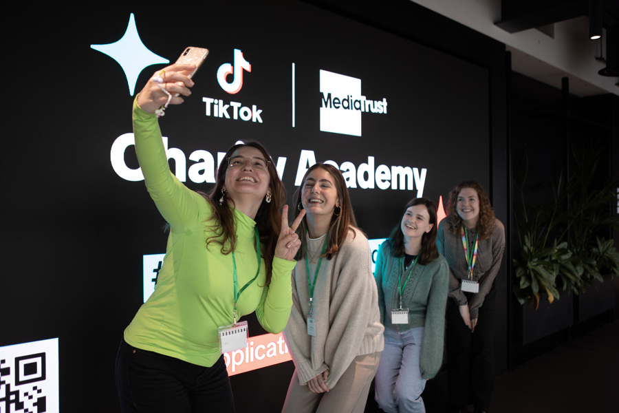 People posing for a selfie in front of the TikTok Charity Academy logo.