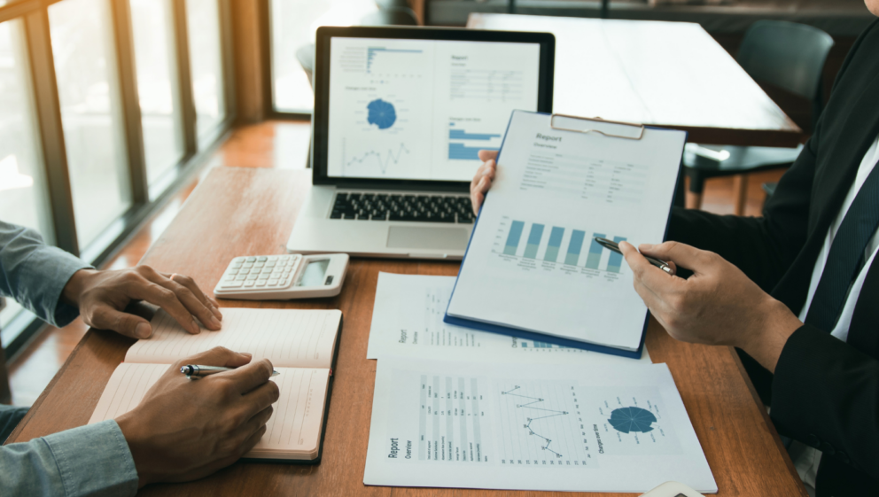 Closeup of two people looking at data on a clipboard, paper and a screen