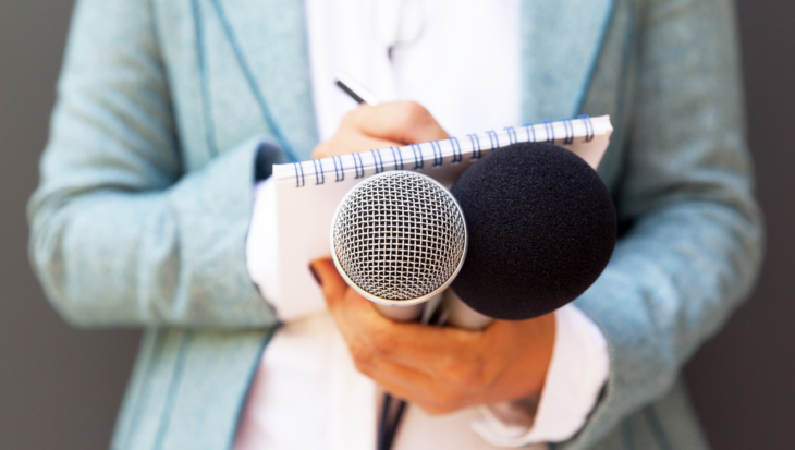 A close-up of a journalist writing in a notebook as they hold a microphone