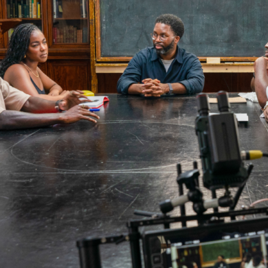 A BTS from the BBU film mandem, showing 5 people sat around a table, in front of a blackboard and bookshelves