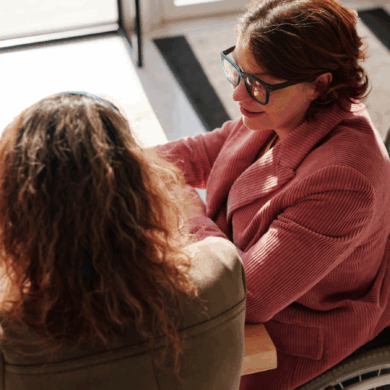 Two people sat, one in a wheelchair, at a desk and looking a laptop
