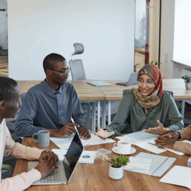 Four young people sat around an office table, with notes and a laptop, working and talking together