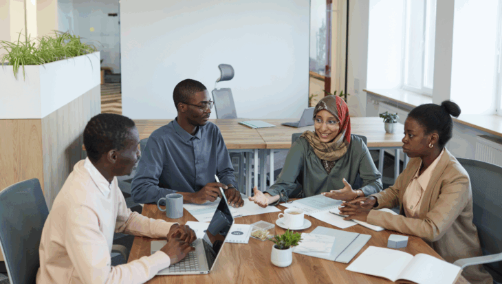 Four young people sat around an office table, with notes and a laptop, working and talking together