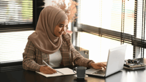 A person taking notes as they look at their laptop