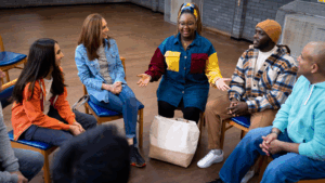 A group of people sat around, in a circle, talking and smiling