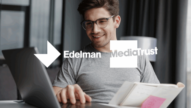 A person using their laptop whilst holding notes and smiling Edelman and Media Trust logos