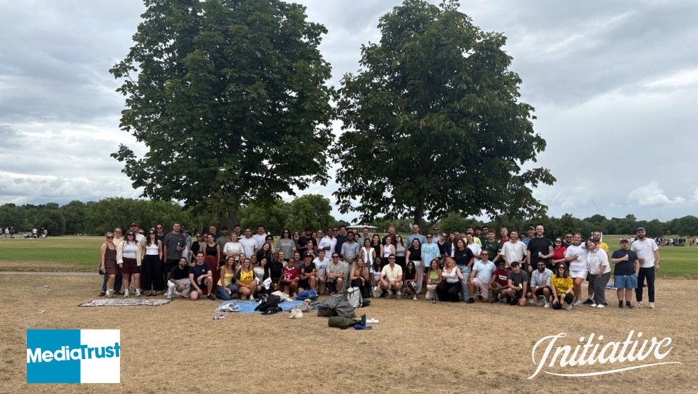 A large group of people stood outside in a park Media Trust and Initiative logos
