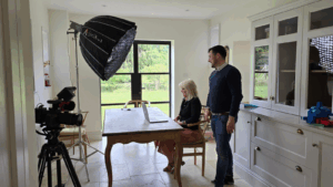 One person sat, at a laptop, with another stood behind them, filming for ADC