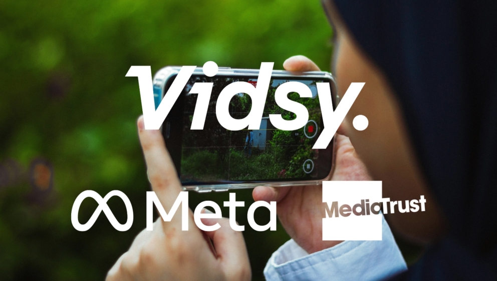 A person, stood outside, filming a video on a mobile phone Logos for Vidsy, Meta and Media Trust