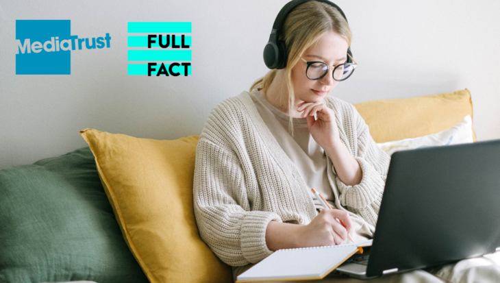 A white woman with tied up blonde hair, black glasses and black headphones sit's on a green sofa with yellow cushions. She is looking at her laptop and notebook.