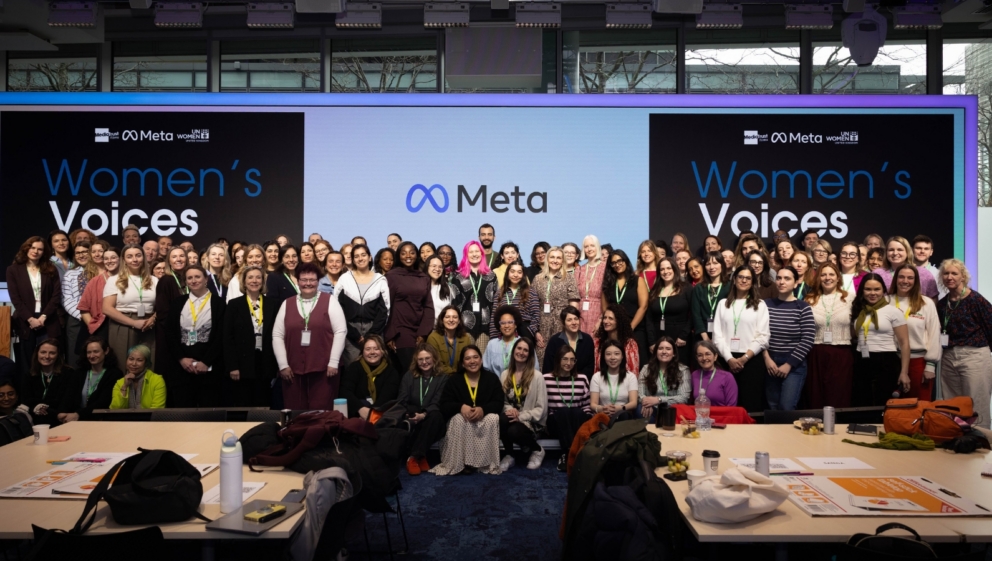 A large group of people stood in front of screens showing logos for Women's Voices, Media Trust Films, Meta and UN Women UK