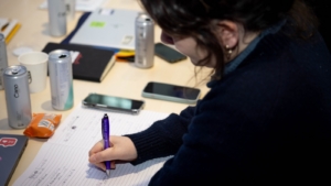A person, sat a table, writing in a notepad