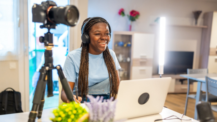 A person sat in front of a laptop, smiling as they record a podcast.