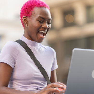 A person with bright pink hair, smiling widely as they use a laptop