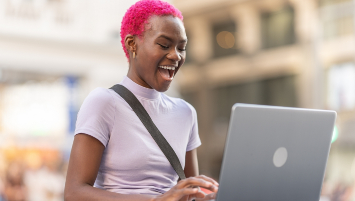 A person with bright pink hair, smiling widely as they use a laptop