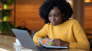 A person making notes as they look at their laptop