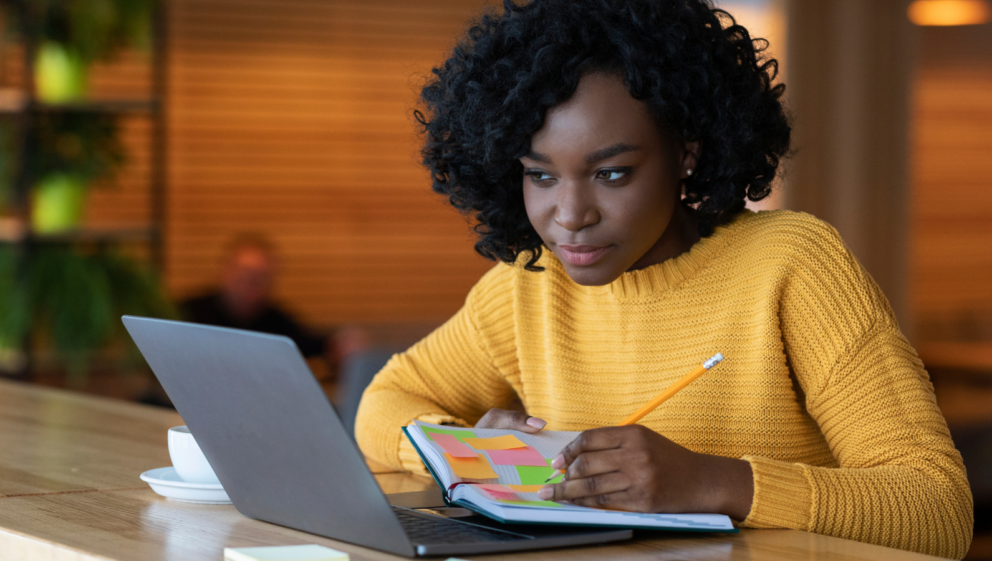A person making notes as they look at their laptop