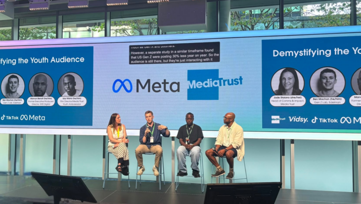 Jade sat on stage with Ben, Izzi and Marvyn. Behind them are screens showing logos for Meta, Media Trust and their headshots.