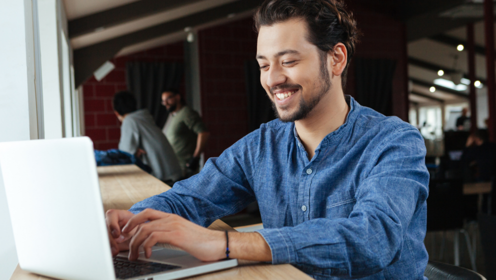 A person smiling as they type on a laptop.