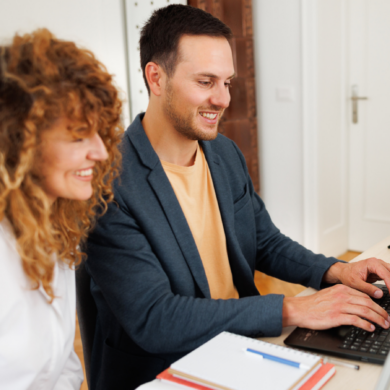 Two people sat a desk, working together on a laptop.