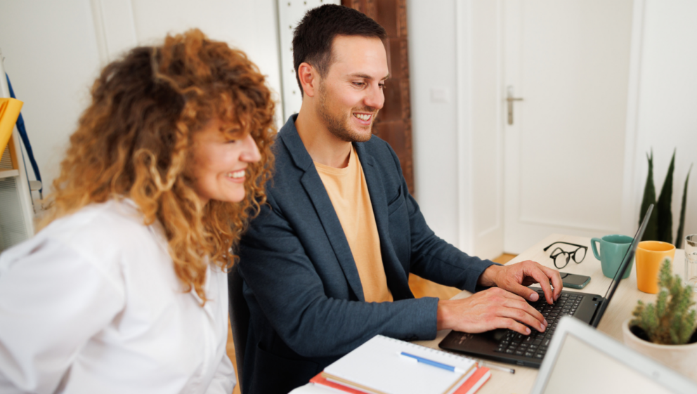 Two people sat a desk, working together on a laptop.